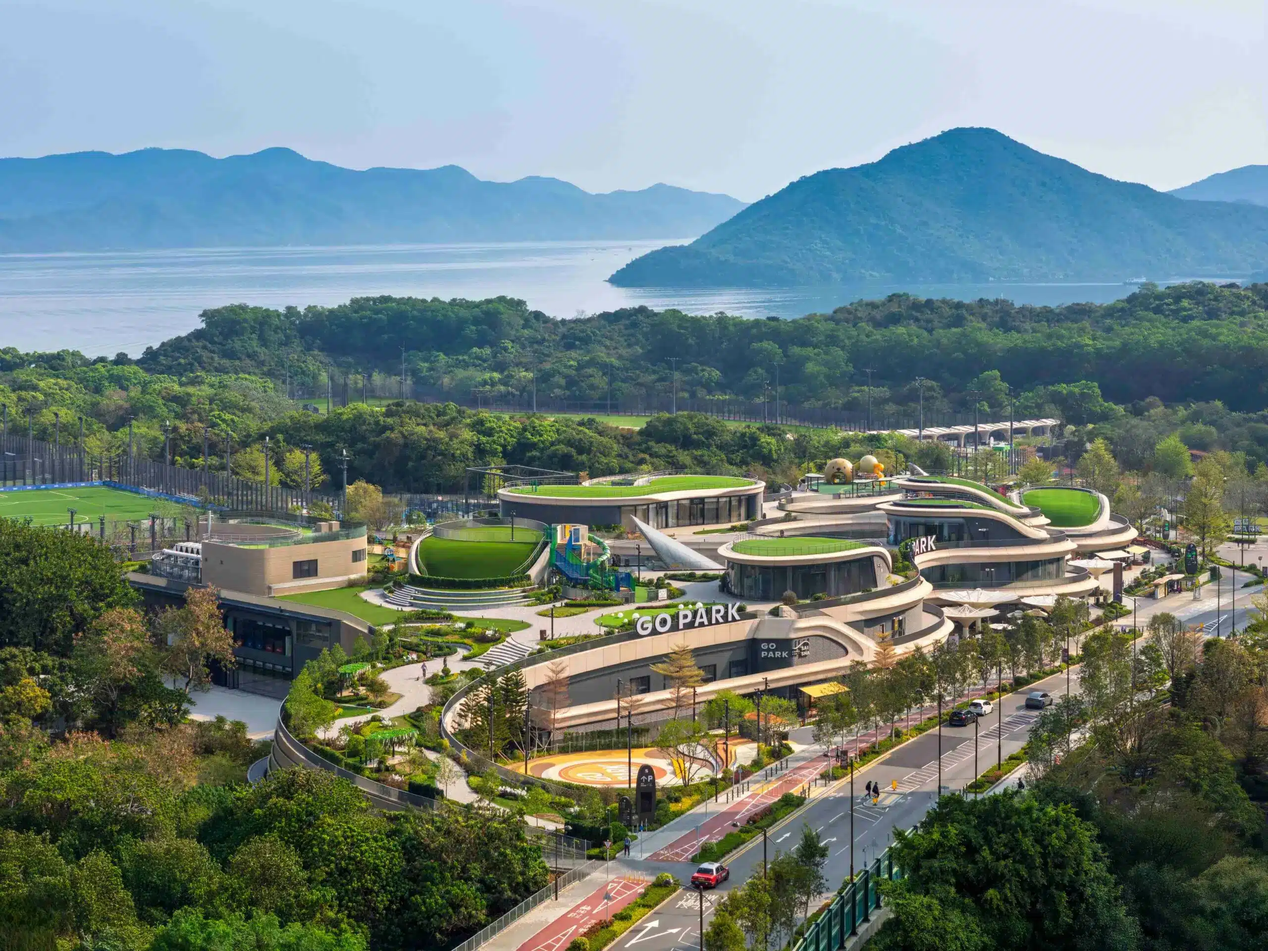Zaha Hadid Architects tarafından tasarlanan GO PARK Sai Sha kompleksinin dalgalı ve akışkan formlarını gösteren geniş açılı bir fotoğraf.